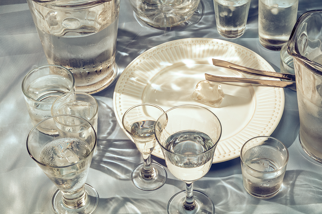 Foto de uma mesa de refeição com vários copos com água e um gelo servido em um prato 