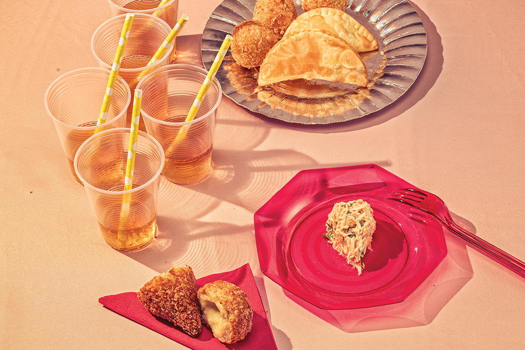 Foto de uma mesa de refeição com várias frituras servidas, com copos com refrigerante ao lado 