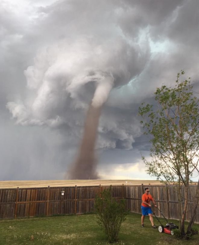 Homem corta grama enquanto tornado passa perto de sua casa