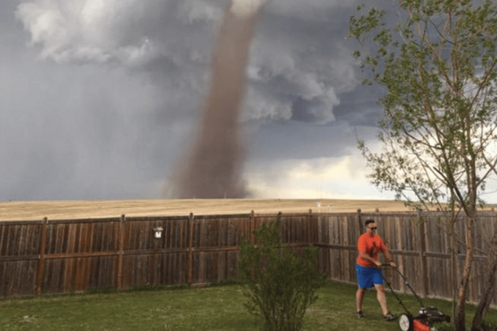 Homem corta grama enquanto tornado passa perto de sua casa