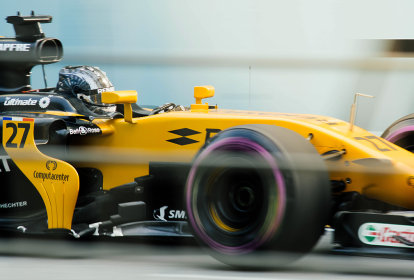 Zoom em um carro de corrida amarelo, com o piloto dentro, em alta velocidade.