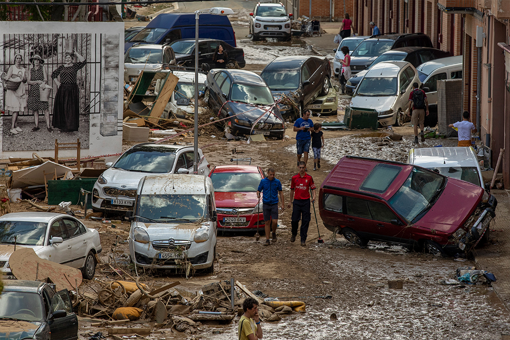 Pessoas andam em meio à lama, escombros e carros tombados por causa da inundação em Tafalla, Espanha.