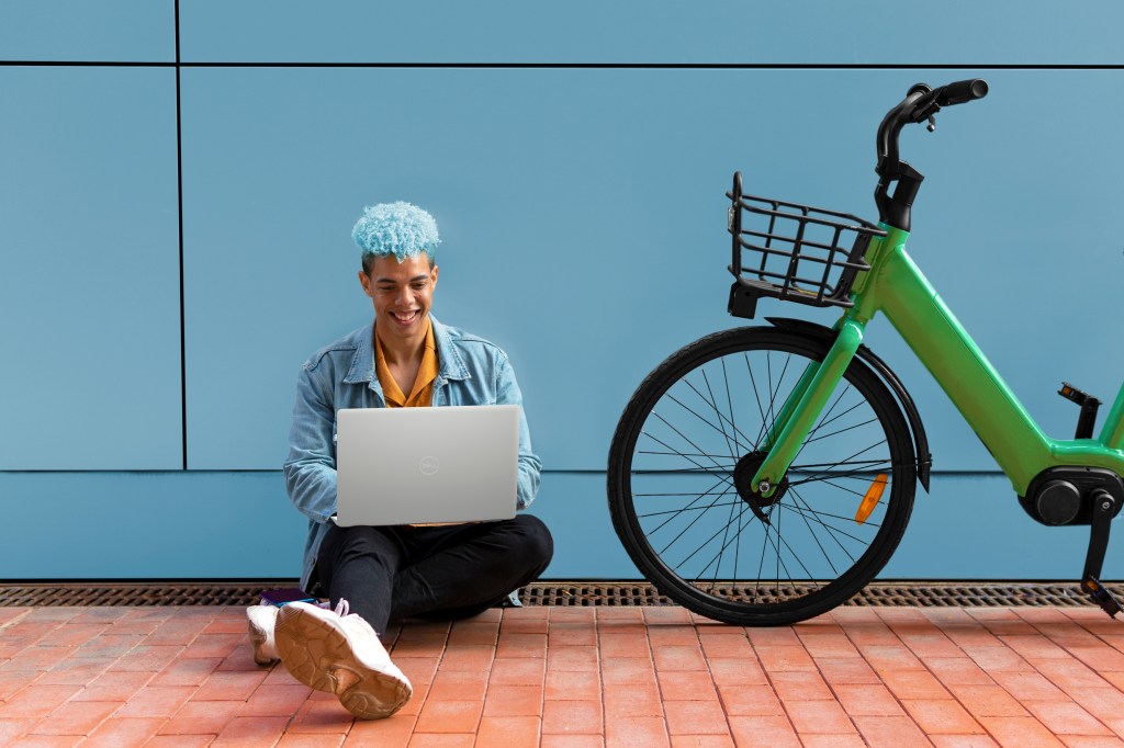 shutterstock_1896084670_with_in3501nt-2 Homem sentado no chão ao lado de bicicleta verde enquanto usa Notebook Dell Inspiron 15 3000 Series.