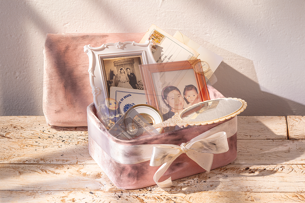 SI_435_Alzheimer_02 Foto de uma caixa de veludo rosa, com um laço em volta. A caixa está suja de carvão e têm vários objetos dentro dela: um espelho, dois retratos, cartas, uma certidão de nascimento, um pratinho decorativo, uma matriosca, um relógio e uma fita cassete. Alguns desses objetos estão desaparecendo.
