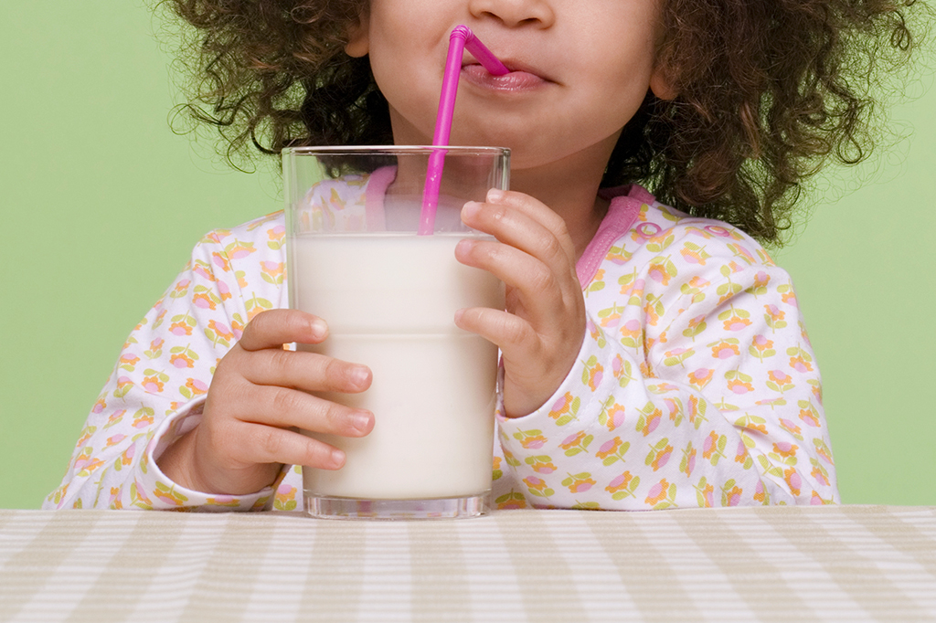 Foto de uma criança tomando leite de um copo com canudinho.