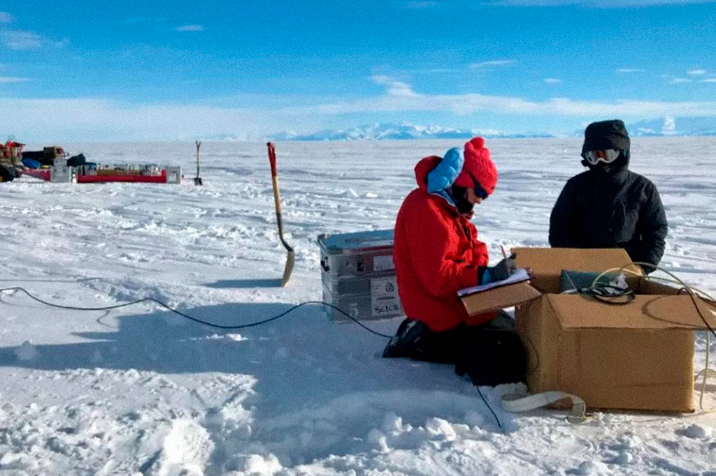 Cientistas manuseando equipamentos na neve, na Antártida.
