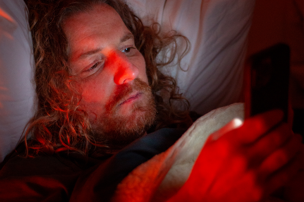 Homem mexendo no celular na cama.