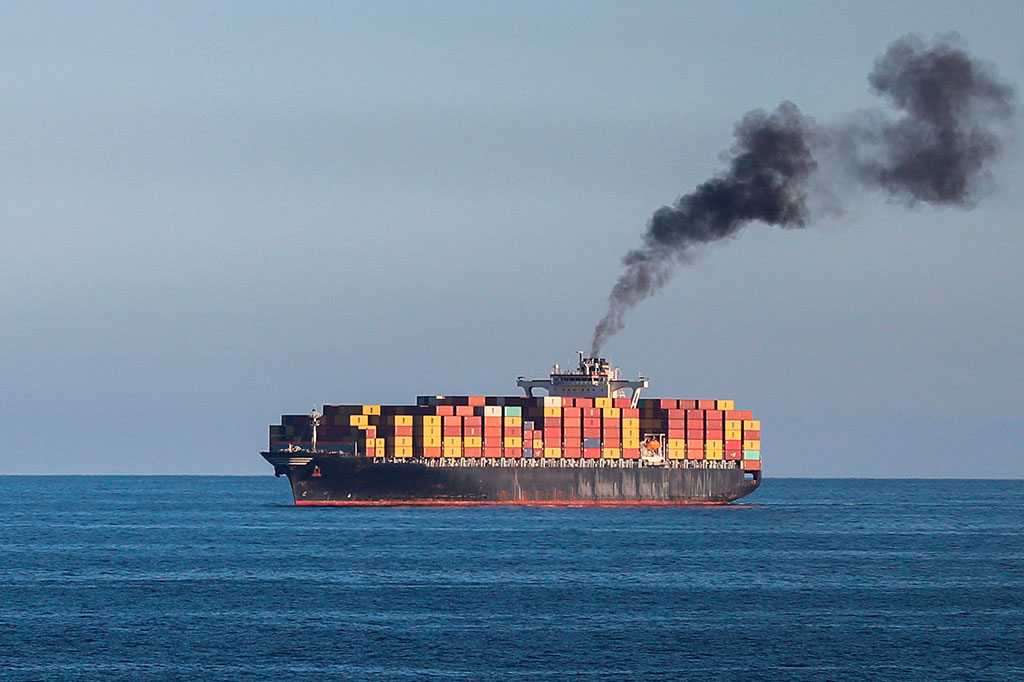 Um grande navio de carga à distância fumando fumaça preta.
