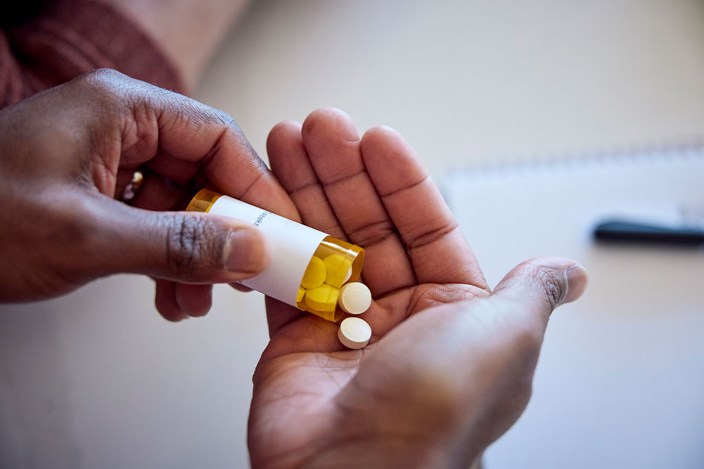 Foto aproximada de um homem derramando medicamentos de um frasco na mão.