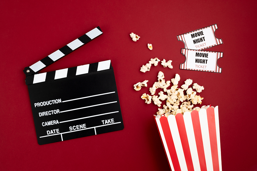 Composição com uma claquete, balde de pipoca e ingressos de cinema em fundo vermelho.