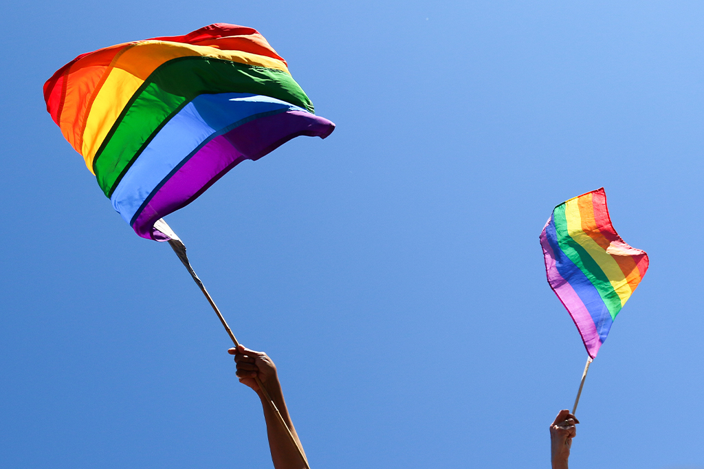 Close das mãos de duas pessoas balançando bandeiras LGBT.
