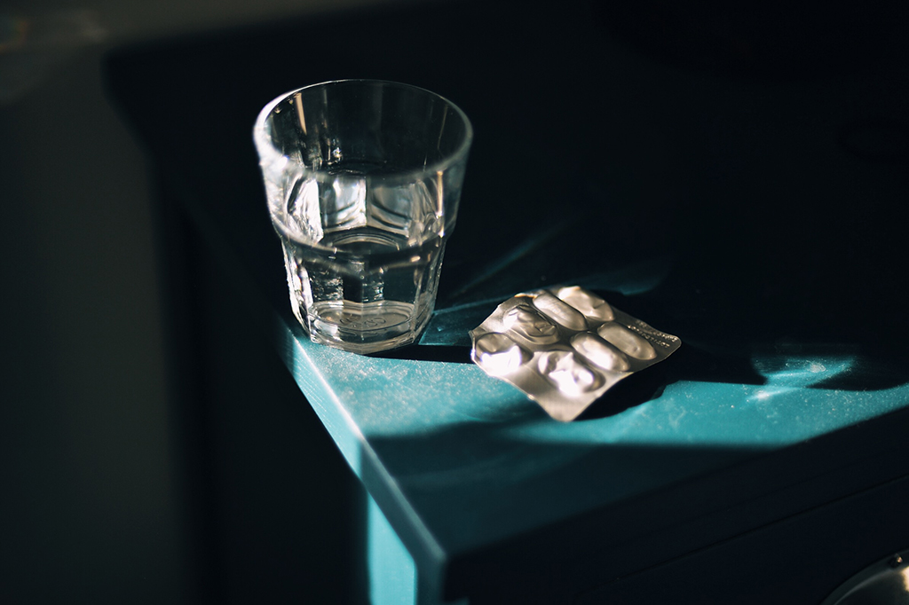 Um copo de vidro em cima de um armário ao lado de uma cartela de remédios.