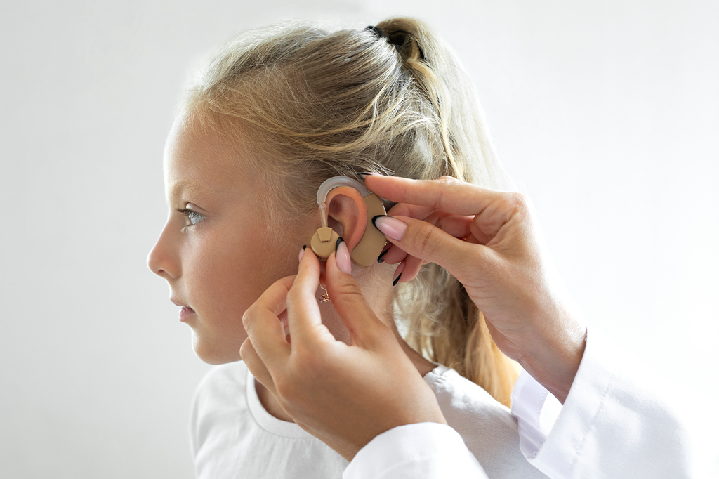 Médico colocando um aparelho auditivo no ouvido de uma criança.