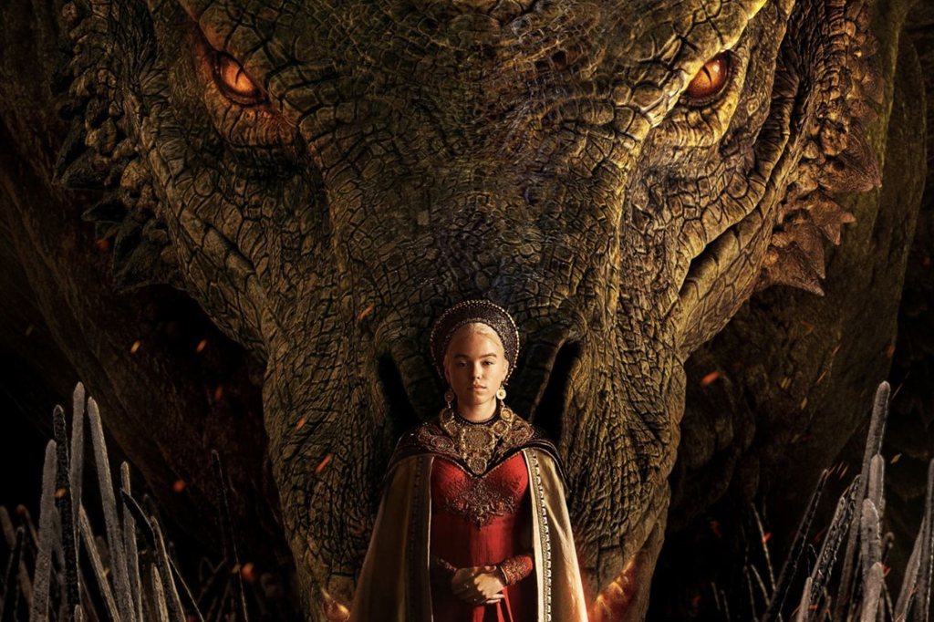 House of The Dragon (2022). Há uma mulher vestida de realeza, com um vestido e uma capa. Atrás dela, há um enorme dragão.