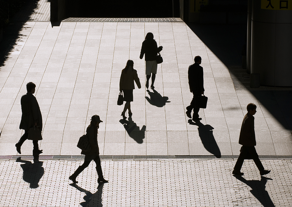 Pessoas andando na rua escondidas pela sombra do Sol.