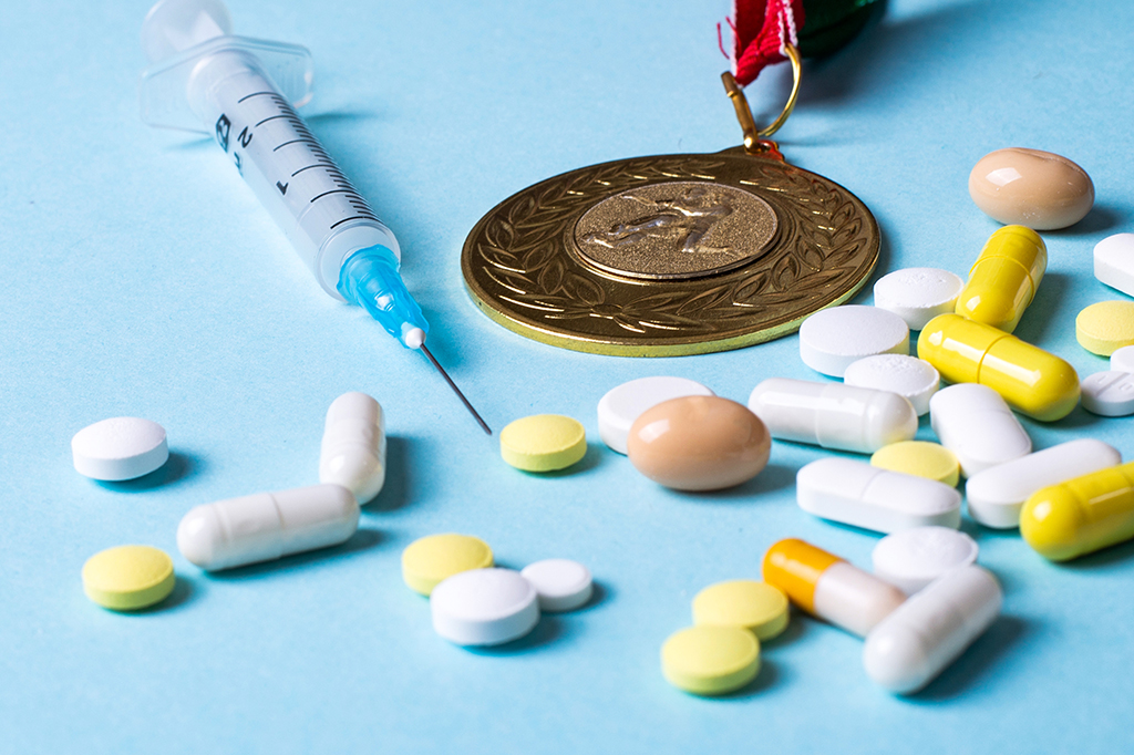 Uma seringa, pílulas e uma medalha dispostas em um fundo azul claro.