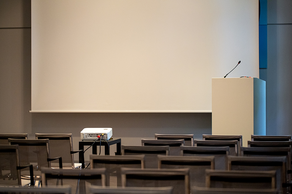Auditório vazio, com cadeiras alinhadas em frente a um palco.