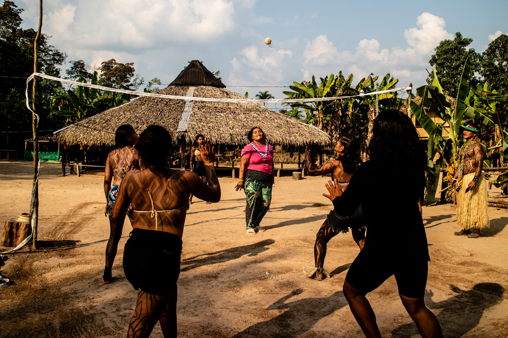 Foto de turistas jogando v&ocirc;lei ind&iacute;gena com uma peteca feita de palha.