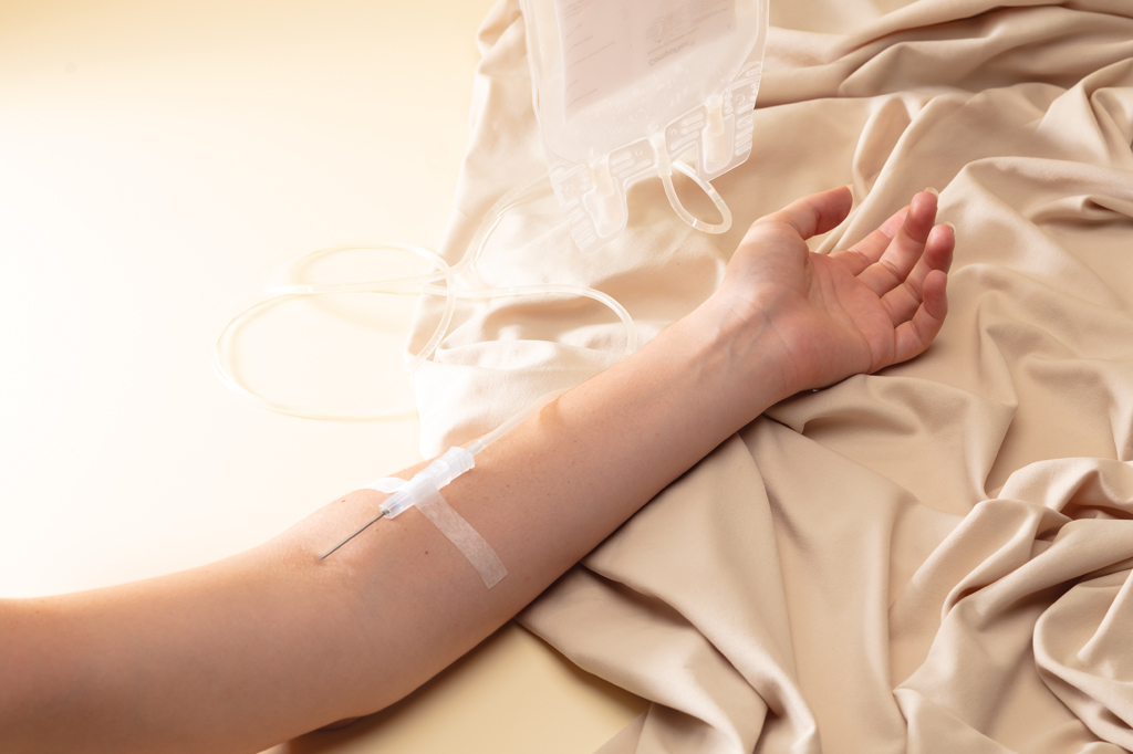 Imagem focada no bra&ccedil;o de uma mulher recebendo medica&ccedil;&atilde;o na veia.