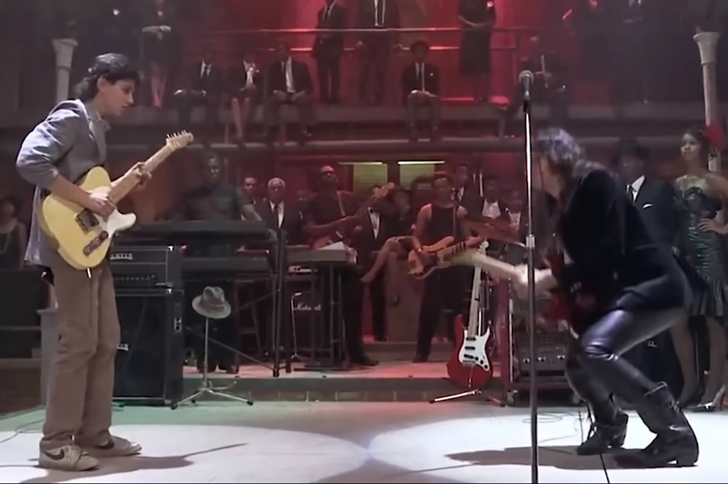 Imagem de um dois guitarristas tocando num palco sendo observados pela plateia. Cena do filme A encruzilhada (1986).
